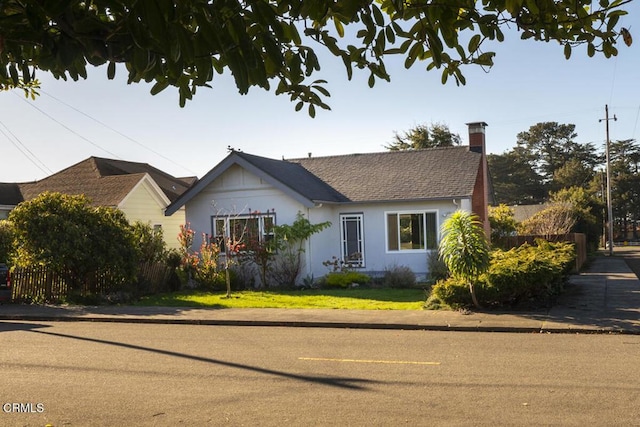 view of front of house with a chimney, fence, a front lawn, and roof with shingles