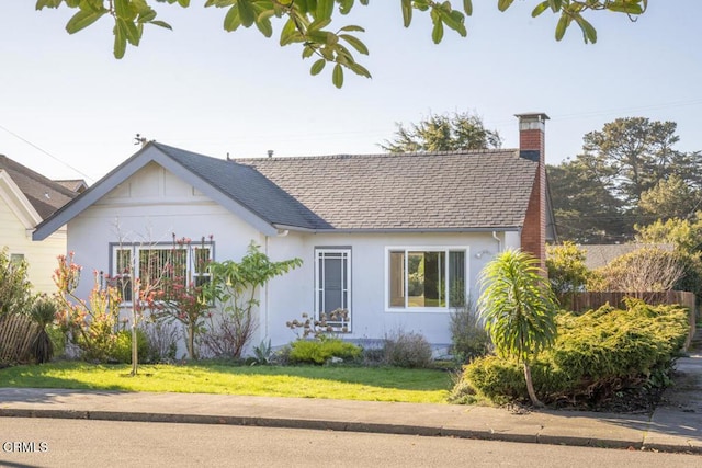 view of front of property featuring roof with shingles, a chimney, stucco siding, a front yard, and fence