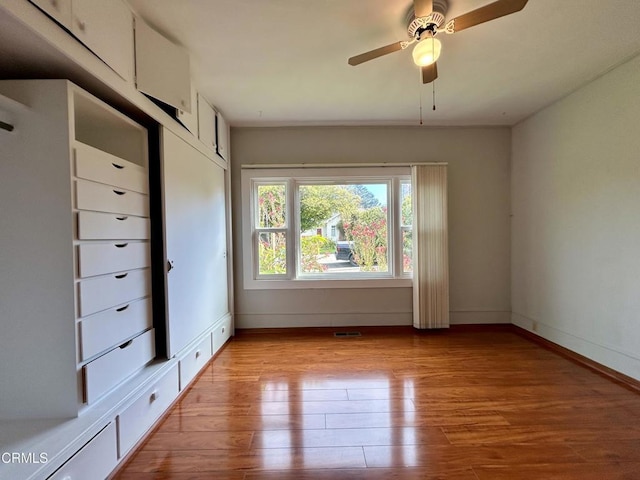 empty room featuring light wood-style flooring, a ceiling fan, visible vents, and baseboards