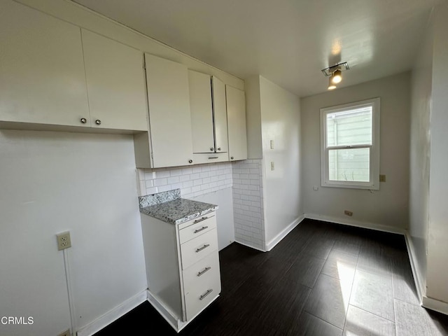 kitchen featuring light stone counters, white cabinetry, baseboards, decorative backsplash, and dark wood finished floors