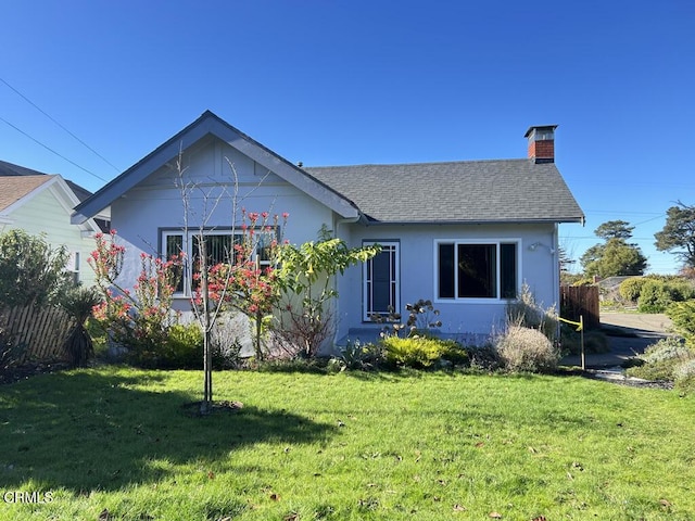 view of front of house with a shingled roof, fence, stucco siding, a chimney, and a front yard