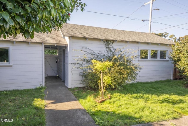 exterior space with roof with shingles and a lawn