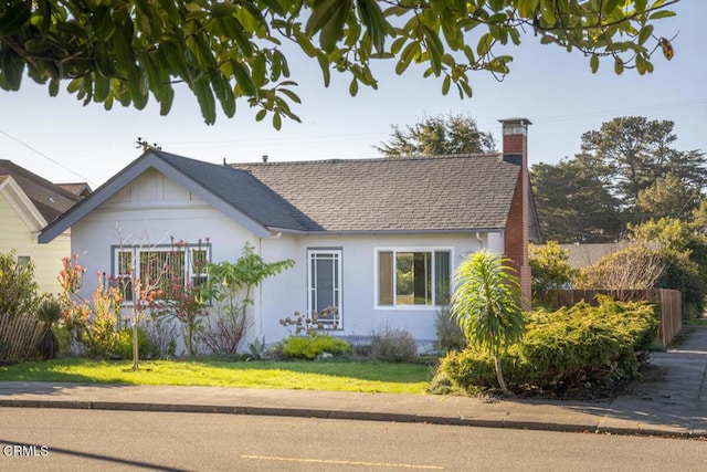 view of front of home with fence, roof with shingles, stucco siding, a chimney, and a front yard