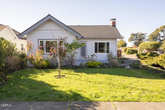 view of front of home featuring a shingled roof, a chimney, and a front yard