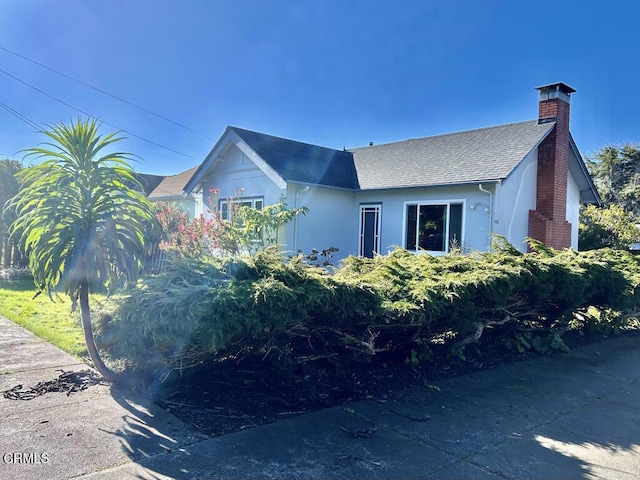 view of front of house with a shingled roof, a chimney, and stucco siding