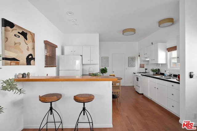 kitchen with white cabinetry, a kitchen bar, white appliances, and kitchen peninsula