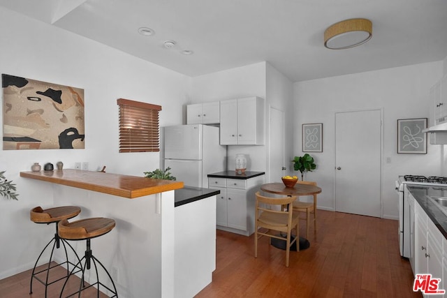 kitchen featuring white cabinetry, white appliances, a breakfast bar area, and dark wood-type flooring