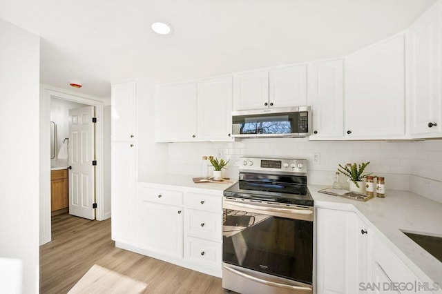 kitchen with stainless steel appliances, tasteful backsplash, white cabinets, and light wood-type flooring