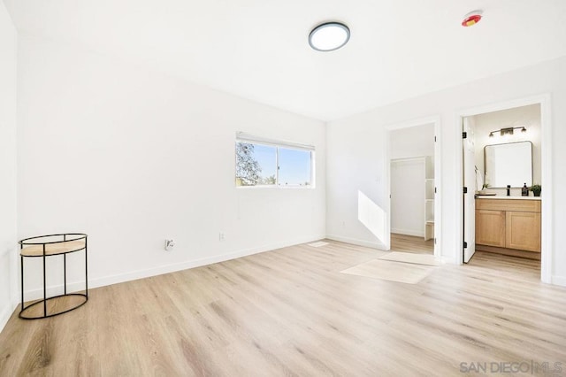 unfurnished bedroom featuring a spacious closet, ensuite bath, and light hardwood / wood-style flooring