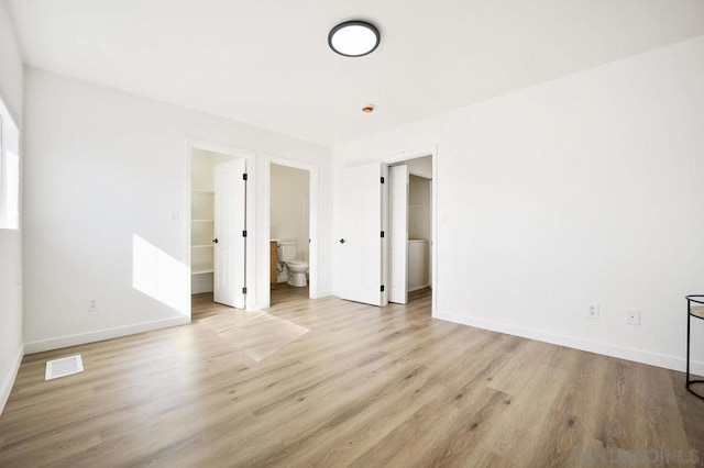 unfurnished bedroom with ensuite bath, light wood-type flooring, and a walk in closet