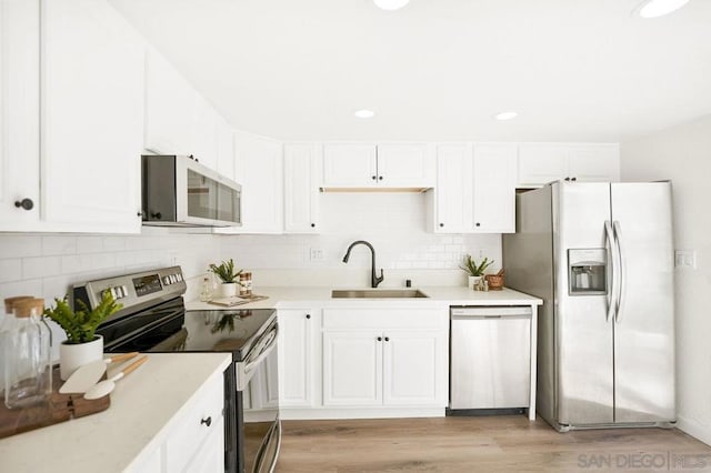 kitchen featuring sink, white cabinetry, tasteful backsplash, light hardwood / wood-style flooring, and appliances with stainless steel finishes