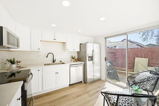 kitchen with sink, light hardwood / wood-style flooring, appliances with stainless steel finishes, white cabinetry, and decorative backsplash