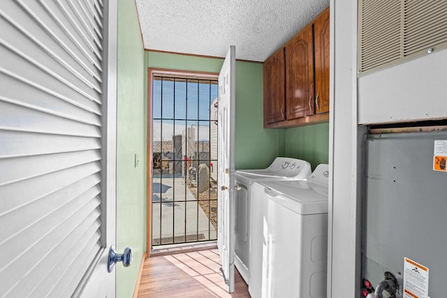 washroom featuring light hardwood / wood-style flooring, washing machine and dryer, cabinets, a water view, and a textured ceiling