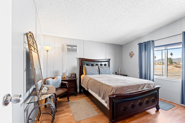 bedroom featuring hardwood / wood-style flooring, a wall unit AC, and a textured ceiling