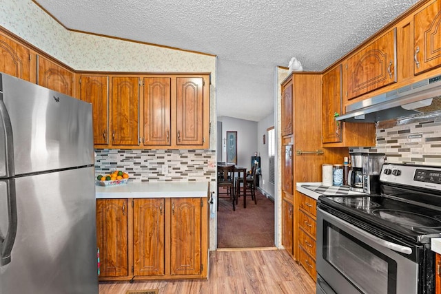 kitchen featuring vaulted ceiling, light wood-type flooring, decorative backsplash, stainless steel appliances, and a textured ceiling