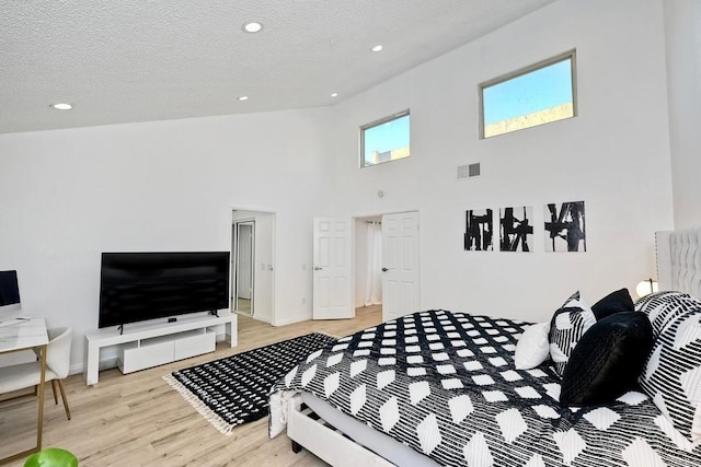 bedroom featuring a high ceiling, a textured ceiling, and light wood-type flooring