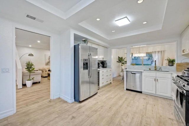 kitchen with sink, light hardwood / wood-style flooring, appliances with stainless steel finishes, a tray ceiling, and white cabinets