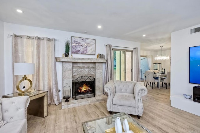 living room with a tiled fireplace, a notable chandelier, and light hardwood / wood-style floors