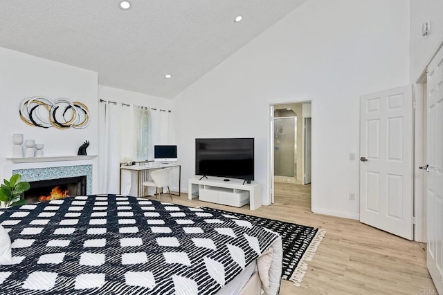 bedroom with baseboards, high vaulted ceiling, light wood-style flooring, a fireplace, and a textured ceiling