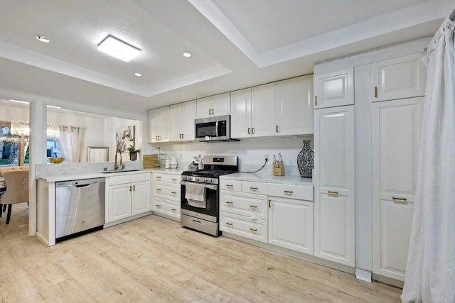 kitchen with a tray ceiling, appliances with stainless steel finishes, light wood-style floors, white cabinets, and a sink