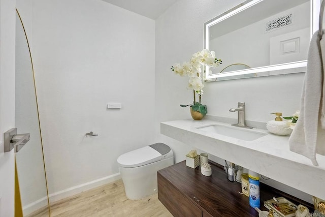 half bath with wood finished floors, baseboards, visible vents, a sink, and toilet