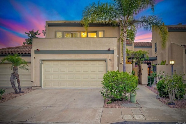 view of front facade featuring stucco siding, driveway, a tile roof, and a garage