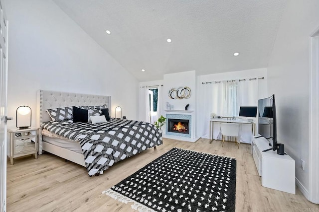 bedroom with a textured ceiling, a lit fireplace, wood finished floors, and vaulted ceiling
