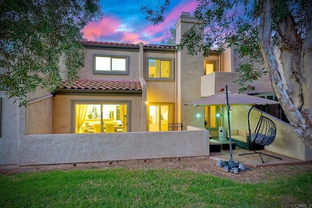 rear view of house featuring a patio, a tiled roof, and stucco siding