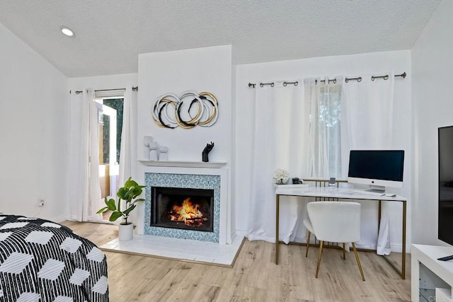 home office with a textured ceiling, wood finished floors, and a tile fireplace