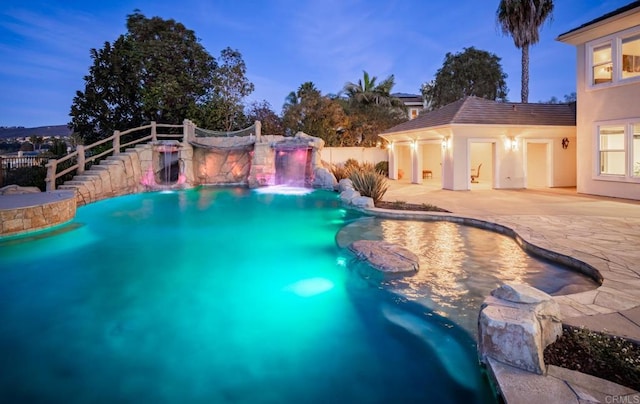 pool at dusk featuring pool water feature, an outdoor structure, and a patio area