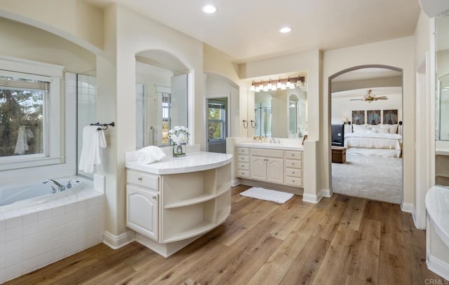 bathroom with hardwood / wood-style flooring, vanity, a relaxing tiled tub, and ceiling fan