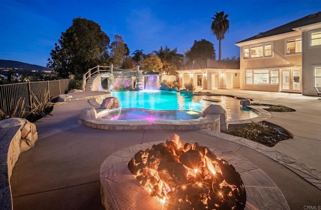 pool at night with pool water feature, a patio area, and a fire pit