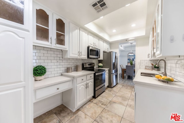 kitchen with sink, appliances with stainless steel finishes, white cabinetry, backsplash, and a tray ceiling