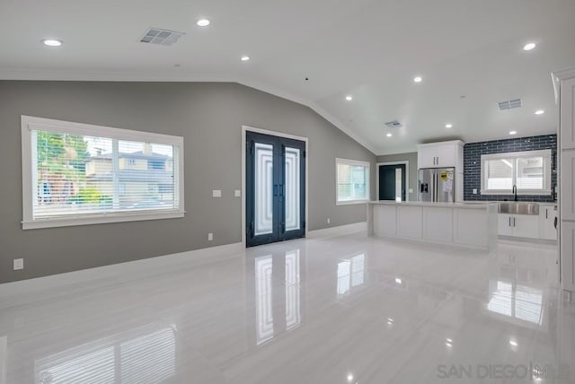 kitchen with lofted ceiling, a wealth of natural light, stainless steel fridge, and white cabinets