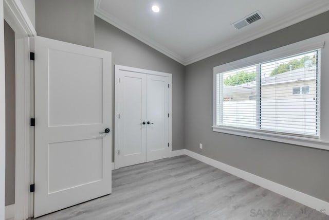 unfurnished bedroom with crown molding, lofted ceiling, light wood-type flooring, and a closet