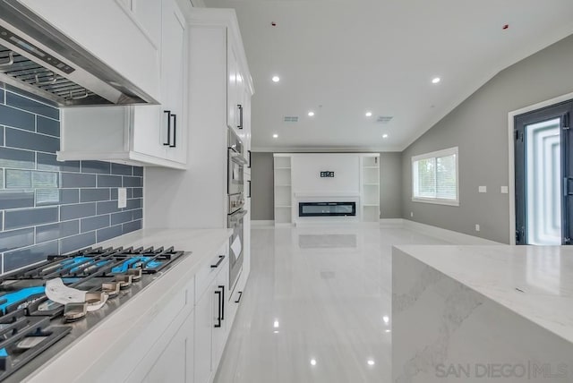 kitchen featuring lofted ceiling, light stone counters, custom range hood, white cabinets, and stainless steel gas stovetop