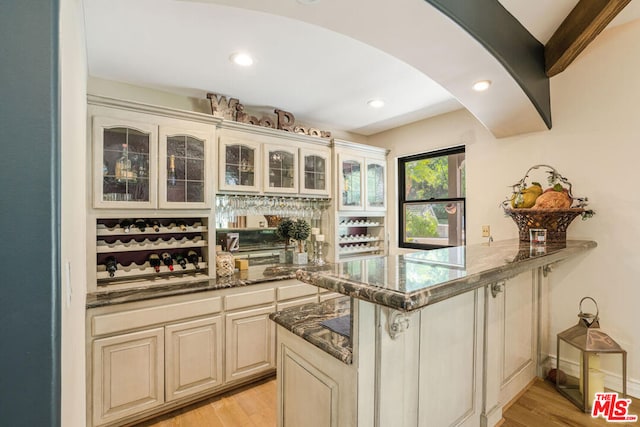 bar featuring dark stone countertops, light hardwood / wood-style floors, and cream cabinetry