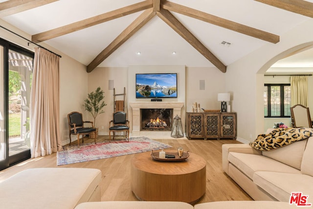 living room with a fireplace, lofted ceiling with beams, and light wood-type flooring