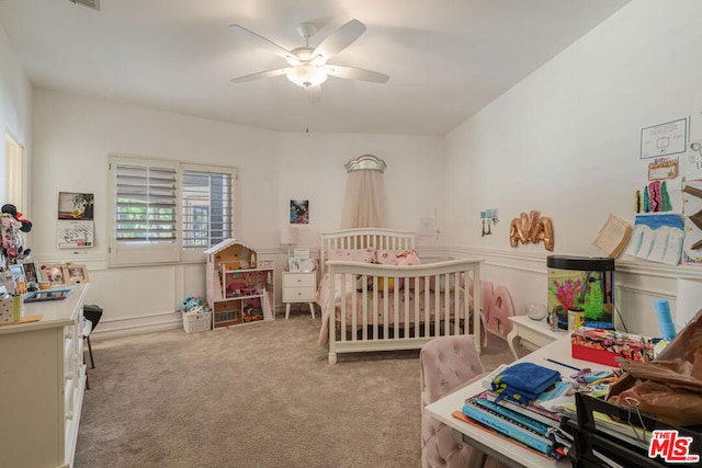 carpeted bedroom featuring a nursery area and ceiling fan