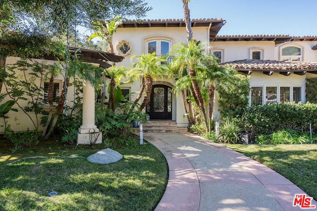 mediterranean / spanish home with a front lawn and french doors