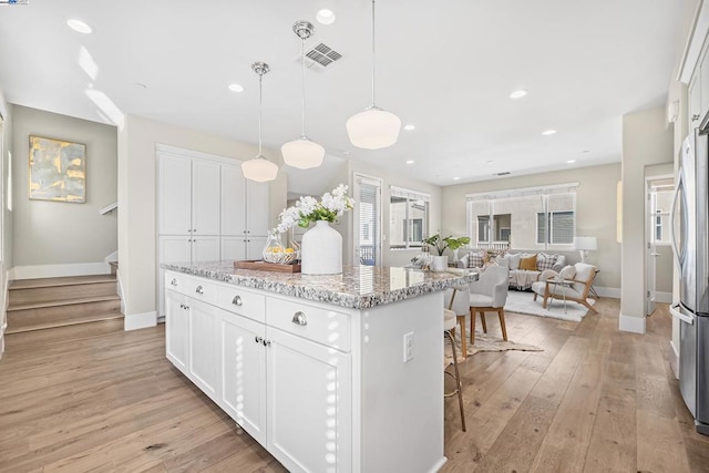 kitchen with white cabinetry, light stone counters, light hardwood / wood-style flooring, a kitchen island, and pendant lighting