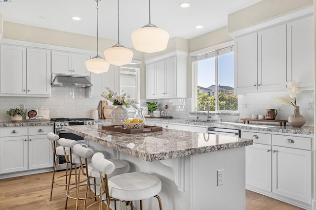 kitchen with white cabinetry, decorative backsplash, stainless steel gas range, and a center island