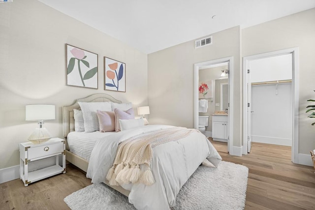 bedroom featuring a walk in closet, connected bathroom, a closet, and light hardwood / wood-style flooring