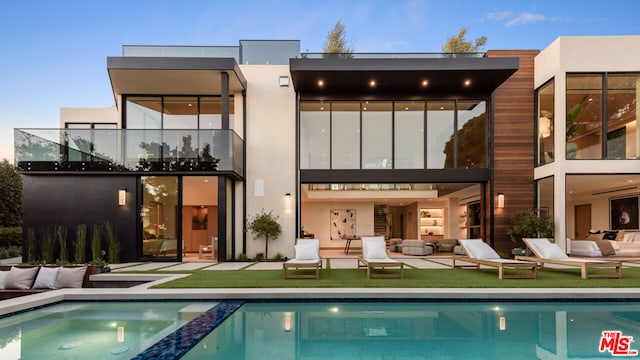 back house at dusk with an outdoor living space and a lawn