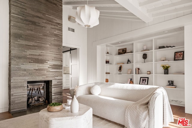 living room featuring a tile fireplace, high vaulted ceiling, wood-type flooring, a barn door, and beamed ceiling