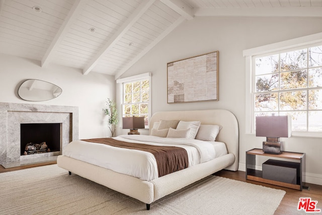 bedroom featuring wood-type flooring, a high end fireplace, multiple windows, and vaulted ceiling with beams