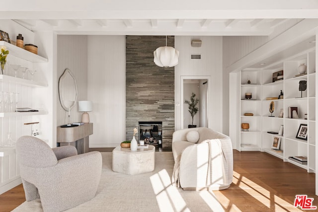 living room with a tiled fireplace, wood-type flooring, beam ceiling, and built in shelves