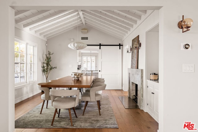 dining area featuring a premium fireplace, a barn door, vaulted ceiling with beams, and light hardwood / wood-style flooring