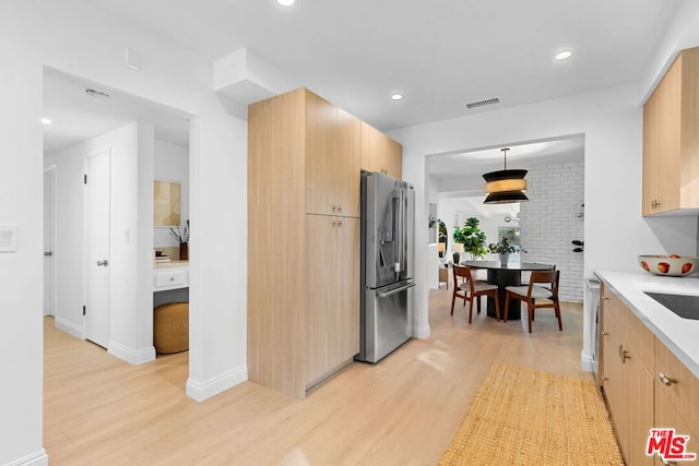 kitchen with light brown cabinetry, light wood-type flooring, brick wall, and appliances with stainless steel finishes