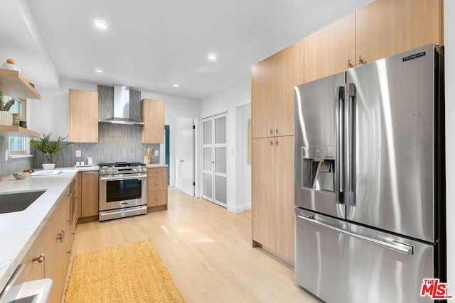 kitchen with light brown cabinetry, tasteful backsplash, wall chimney exhaust hood, and appliances with stainless steel finishes